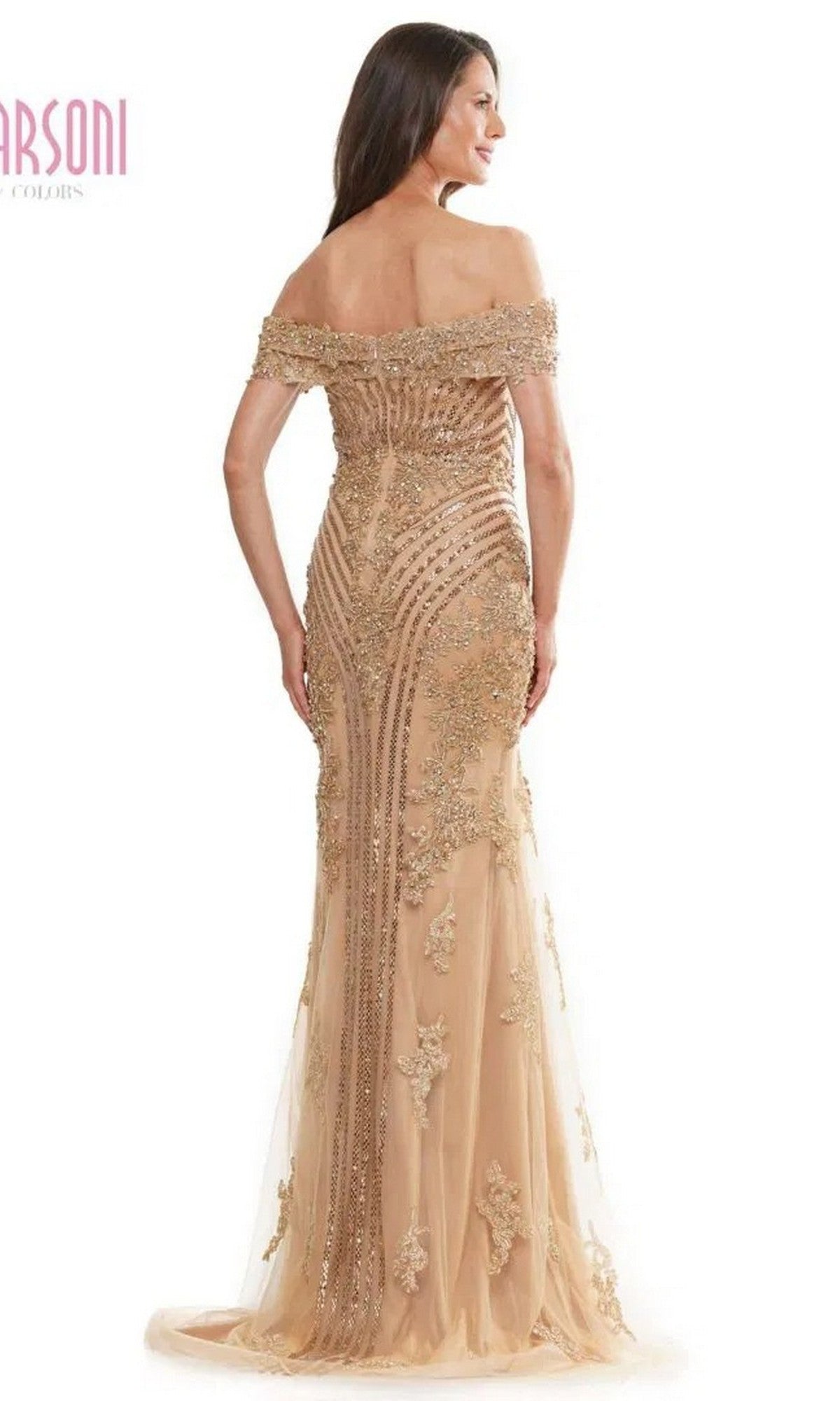 A woman faces away, wearing the Marsoni MV1275 long formal dress featuring an off-the-shoulder neckline, floor-length nude fabric, intricate gold embellishments, and a sheer overlay.